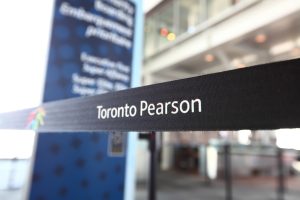 A tape barrier at Toronto Pearson International Airport with "Toronto Pearson" inscription and airport logo on it. Airport premises on the background.